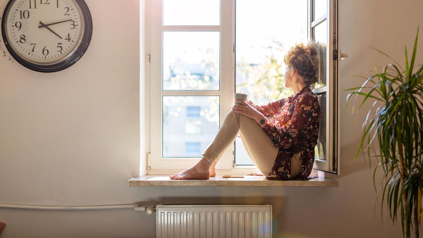 Junge Frau sitzt mit einer Tasse Tee am Fenster und schaut raus