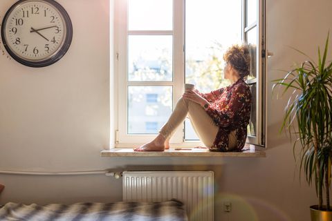 Junge Frau sitzt mit einer Tasse Tee am Fenster und schaut raus