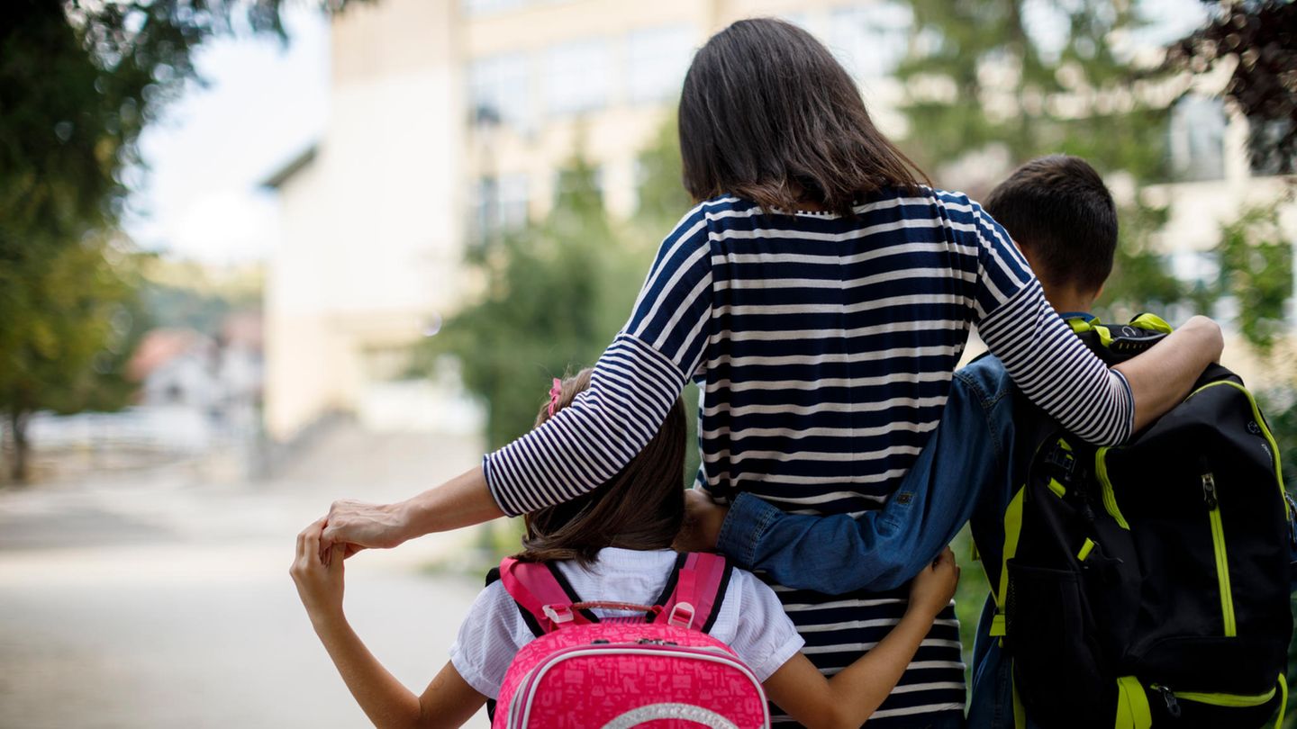 Frau läuft mit zwei Schulkindern im Arm über eine Straße