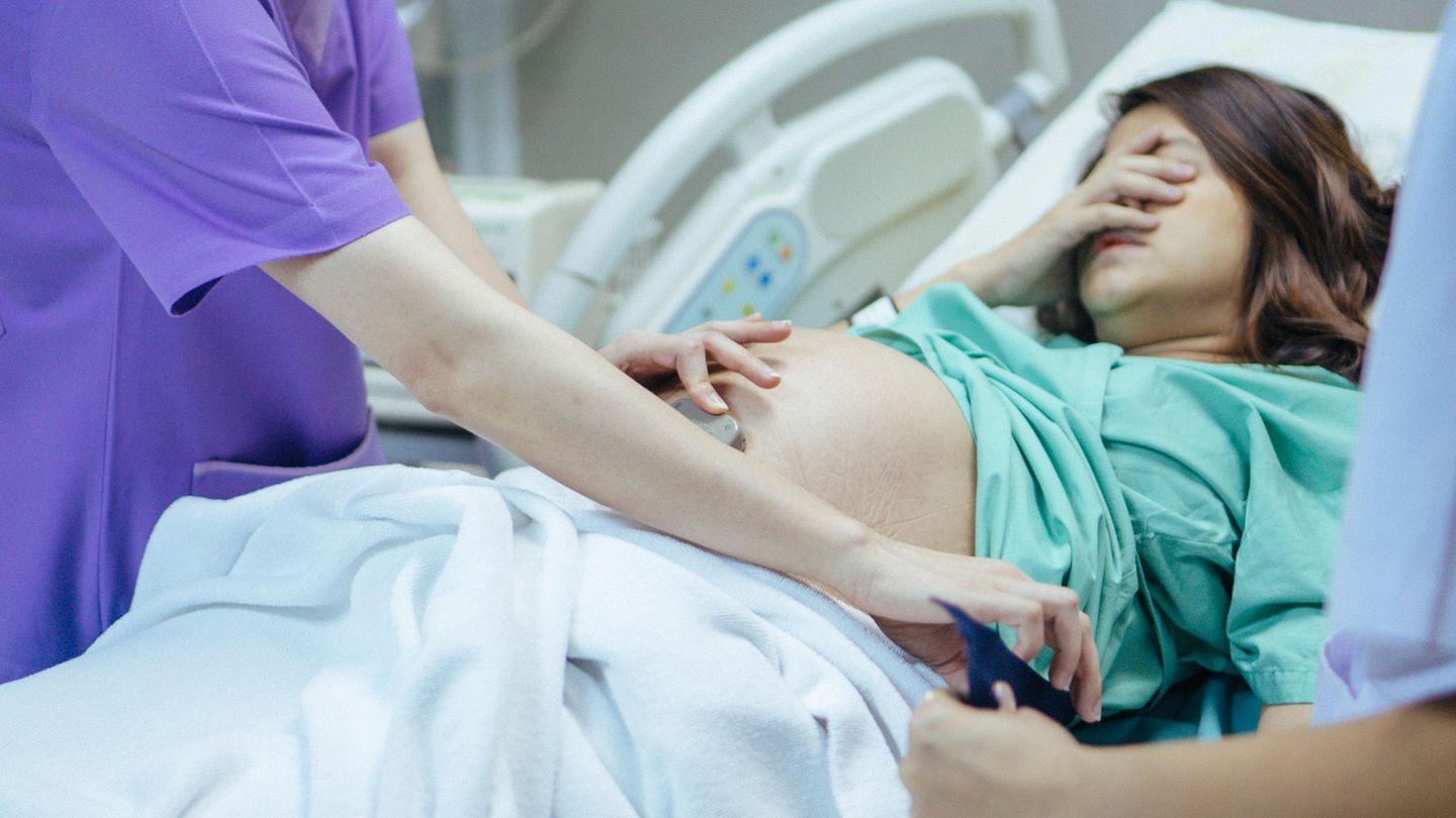 Schwangere Frau liegt im Krankenhausbett und schaut verzweifelt
