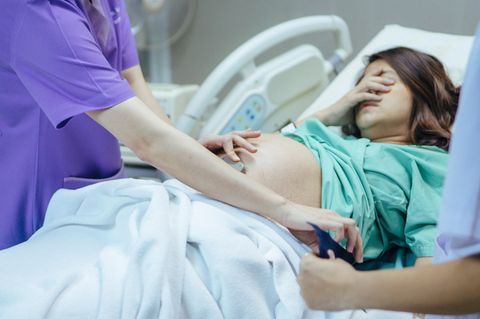 Schwangere Frau liegt im Krankenhausbett und schaut verzweifelt