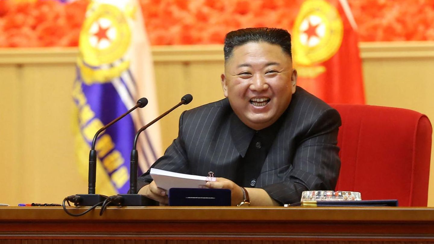 Nordkrieas Diktator Kim Jong Und sitzt an einem Rednerpult und lacht