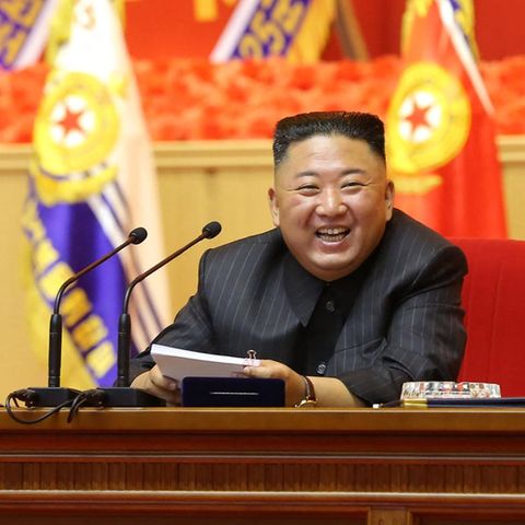 Nordkrieas Diktator Kim Jong Und sitzt an einem Rednerpult und lacht