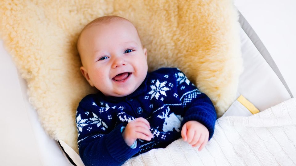 Lammfell im Kinderwagen: Kleiner Junge lacht auf einem Lammfell
