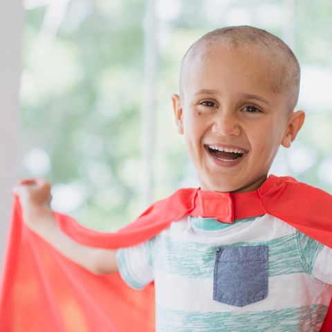 Ein an Krebs erkranktes Kind trägt ein Superman-Cape und lacht