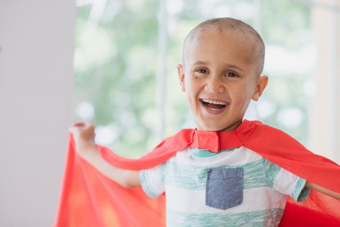Ein an Krebs erkranktes Kind trägt ein Superman-Cape und lacht