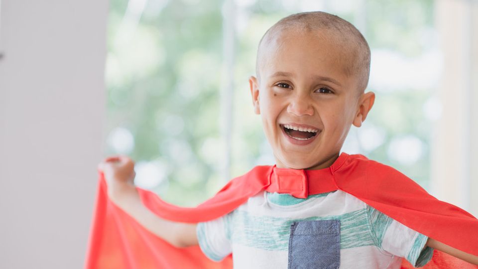 Ein an Krebs erkranktes Kind trägt ein Superman-Cape und lacht