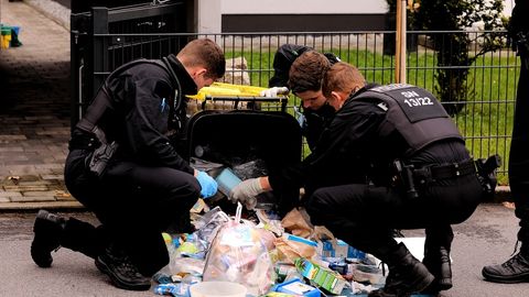 Polizisten durchsuchen in der Umgebung des Tatorts eine Mülltonne