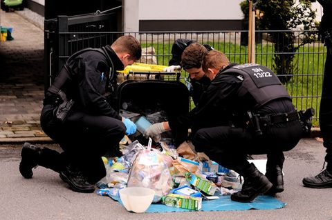 Polizisten durchsuchen in der Umgebung des Tatorts eine Mülltonne