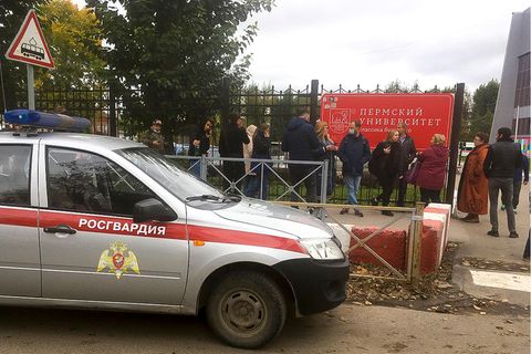 Ein silber-rotes Polizeiauto steht vor einem Metallzaun mit einem roten Schild mit kyrillischer Schrift darauf