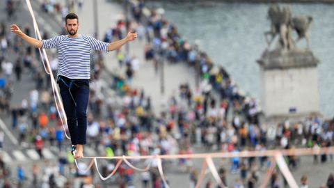 Ein junger weißer Mann mit Vollbart läuft in blau-weißem Ringelshirt auf einem Seil in 70 Metern Höhe