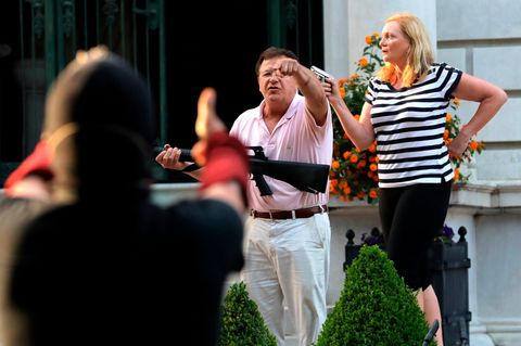 Ein weißer Mann mit weißer Hose und rosa Poloshirt hält ein Sturmgewehr in seinen Händen, eine weiße Frau hält eine Pistole hoch