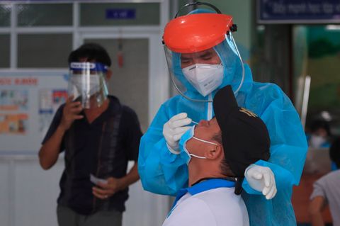 Ein Mitarbeiter im vietnamesischen Gesundheitswesen entnimmt einem Mann einen Abstrich