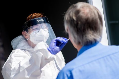 Eine weiße Frau in weißer Schutzkleidung, mit Brille und Gesichtsschirm steckt einem grauhaarigen Mann einen Wattestab
