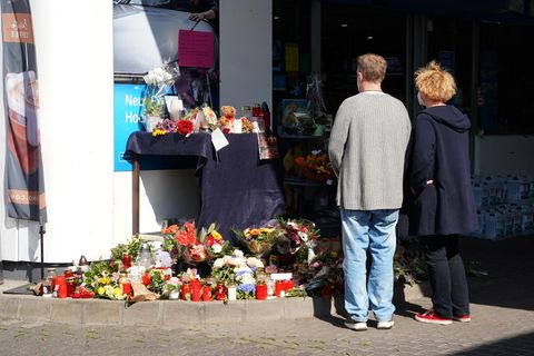 Von hinten sind ein Mann und eine Frau zu sehen, die vor Kerzen und Blumen an einer Tankstelle innehalten