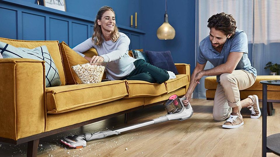 Philips SpeedPro Akku-Staubsauger: Mann saugt Krümel unter einem Sofa auf