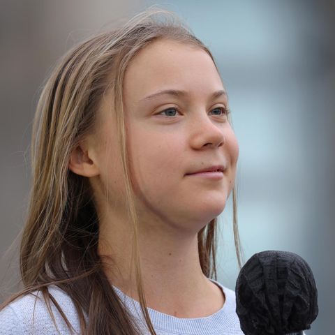Eine junge weiße Frau mit langen, dunkelblonden Haaren lächelt leicht, während sie ein schwarzes Mikro hält