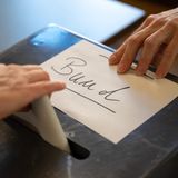 Während eine Hand einen Wahlzettel in eine Wahlurne steckt, zieht eine andere einen Zettel mit "Bund"-Aufschrift vom Schlitz