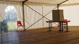 In einem Festzelt mit Holzboden steht eine Wahlkabine, in der gerade ein Mensch steht und wählt