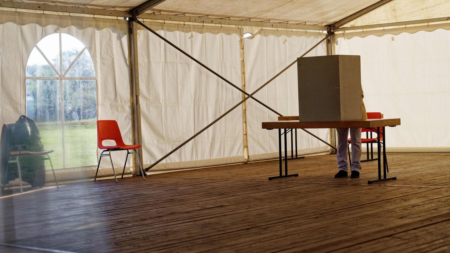 In einem Festzelt mit Holzboden steht eine Wahlkabine, in der gerade ein Mensch steht und wählt