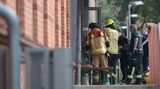 Feuerwehrleute machen sich an der Tür eines rötlichen Backstein-Gebäudes zu schaffen