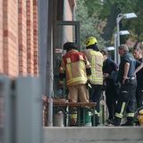 Feuerwehrleute machen sich an der Tür eines rötlichen Backstein-Gebäudes zu schaffen