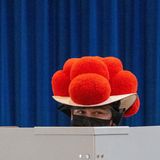 Über den grauen Sichtschutz einer Wahllkabine hinweg sieht man die Augen einer Frau unter der Krempe eines Bollenhutes