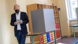 Ein weißer Mann mit Halbglatze, dunkelblauem Jackett und Jeans faltet beim Gehen aus der Wahlkabine einen Zettel