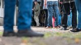 Menschen stehen mit Abstand vor einem Wahllokal Schlange. Wegen des Teleobjektives der Fotografen sind einige Personen unscharf