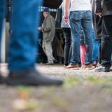 Menschen stehen mit Abstand vor einem Wahllokal Schlange. Wegen des Teleobjektives der Fotografen sind einige Personen unscharf