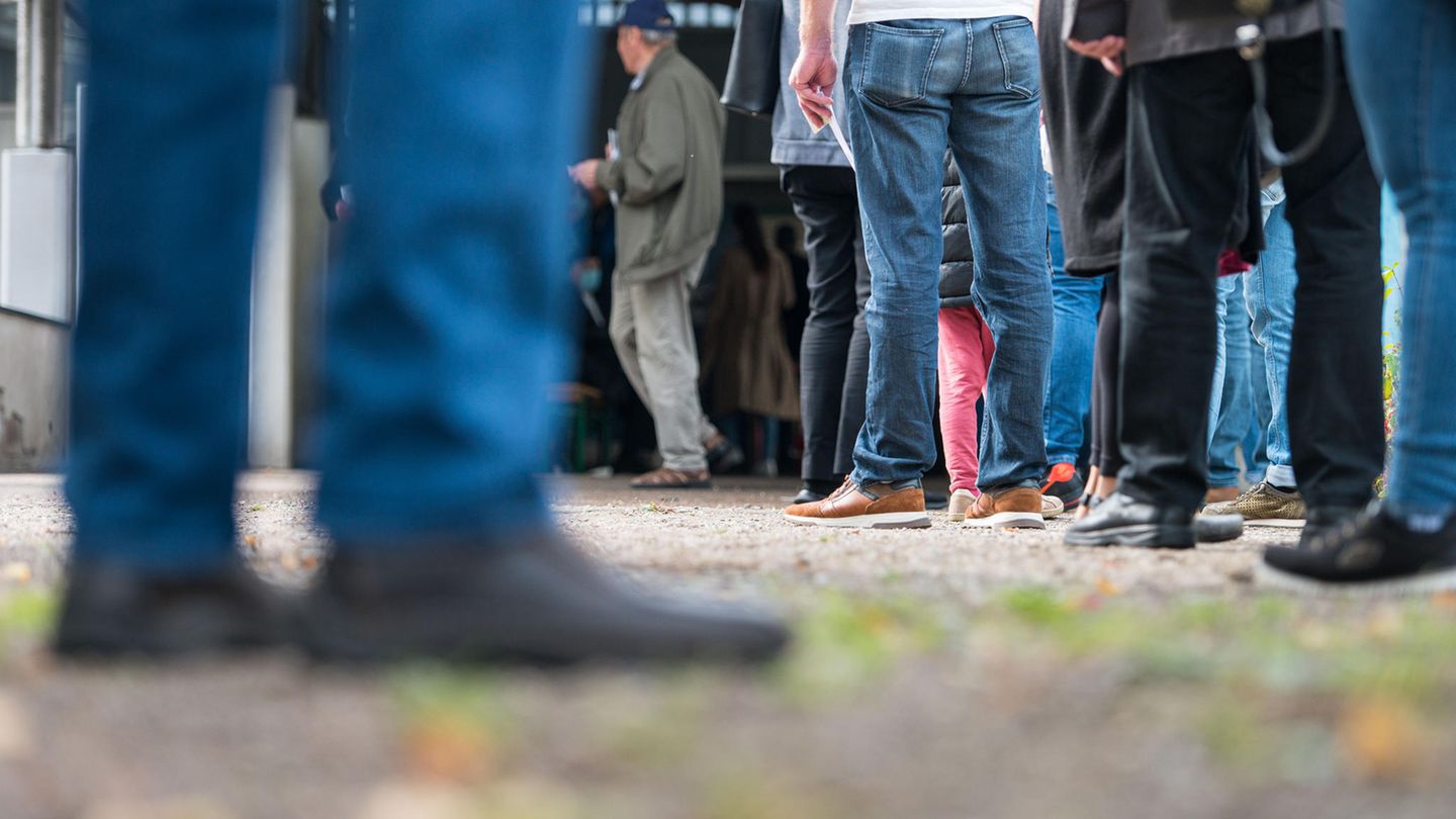 Menschen stehen mit Abstand vor einem Wahllokal Schlange. Wegen des Teleobjektives der Fotografen sind einige Personen unscharf