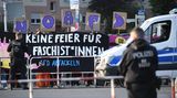 Hinter von Polizisten und rot-weißen Absperrgittern stehen Protestierende mit einem Banner "Keine Feier für Faschist*innen"