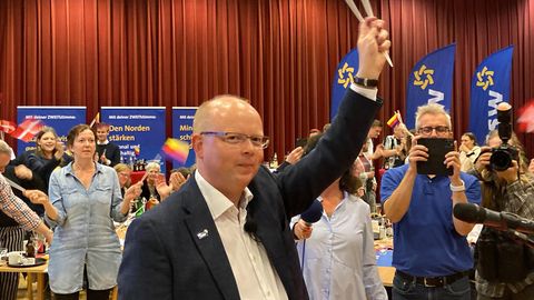 Stefan Seidler schwenkt auf der Wahlparty des SSW Fähnchen mit dem Dannebrog und den friesischen Farben