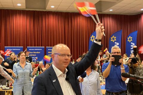 Stefan Seidler schwenkt auf der Wahlparty des SSW Fähnchen mit dem Dannebrog und den friesischen Farben