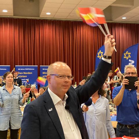 Stefan Seidler schwenkt auf der Wahlparty des SSW Fähnchen mit dem Dannebrog und den friesischen Farben