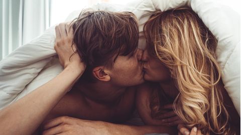 Ein Paar küsst sich unter der Bettdecke im Bett