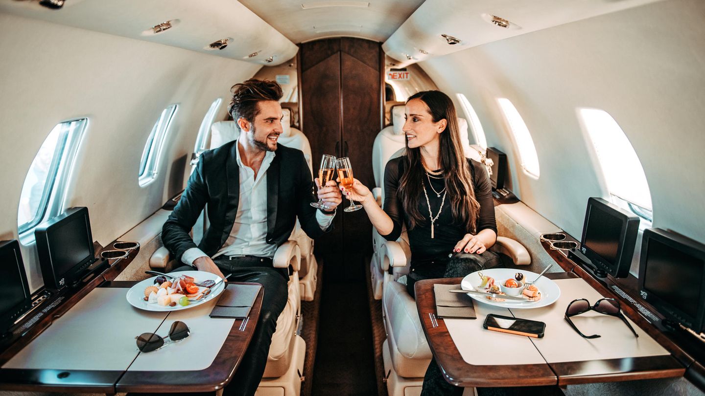 Faktencheck: CO2-Ausstoß Konsumbedingter CO2-Ausstoß: Mann und Frau stoßen in einem Privatjet mit Champagner an