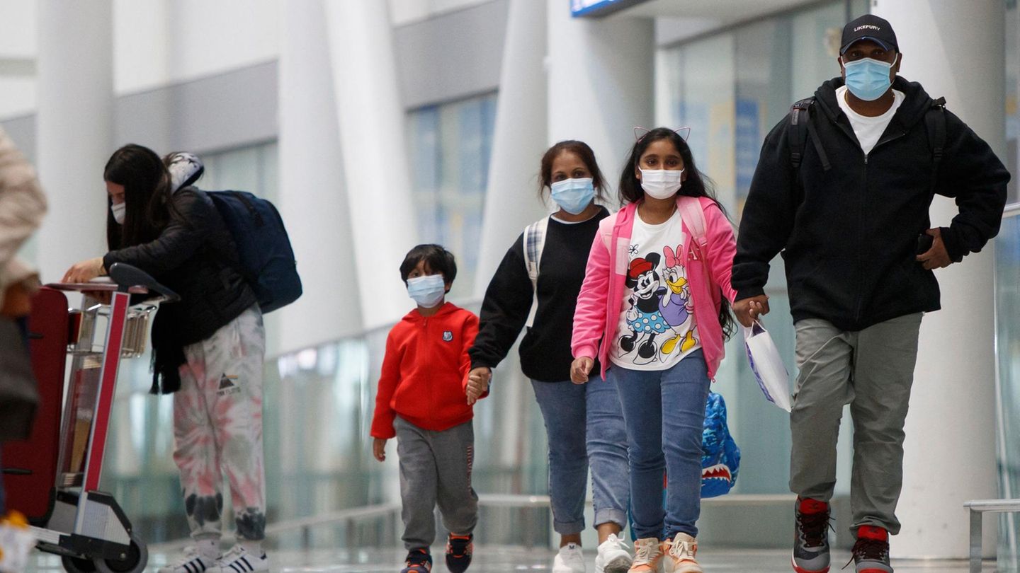 Fünf Personen in Freizeitkleidung und Mundschutz in einem Flughafengebäude