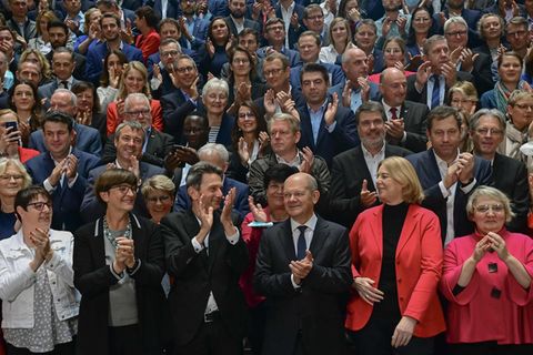 Auf einer Treppe in einem Gebäude stehen lauter meist ältere weiße Männer und Frauen, die gut gekleidet sind