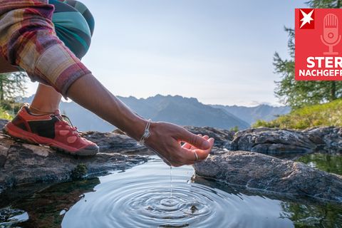 Eine Frau schöpft mit ihrer Hand Wasser aus einem Bergsee