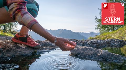 Eine Frau schöpft mit ihrer Hand Wasser aus einem Bergsee