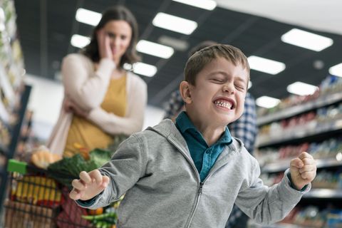 Kleiner Junge beim Einkaufen. Im Hintergrund fast sich seine Mutter an den Kopf.