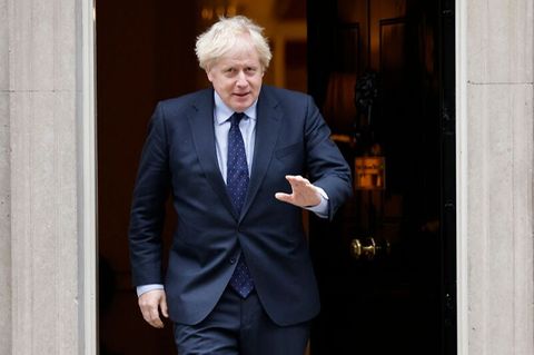 Boris Johnson tritt aus einer Tür heraus und winkt