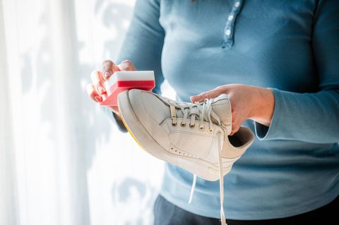 Frau, die weiße Turnschuhe zu Hause mit einem speziellen Reinigungsschwamm reinigt