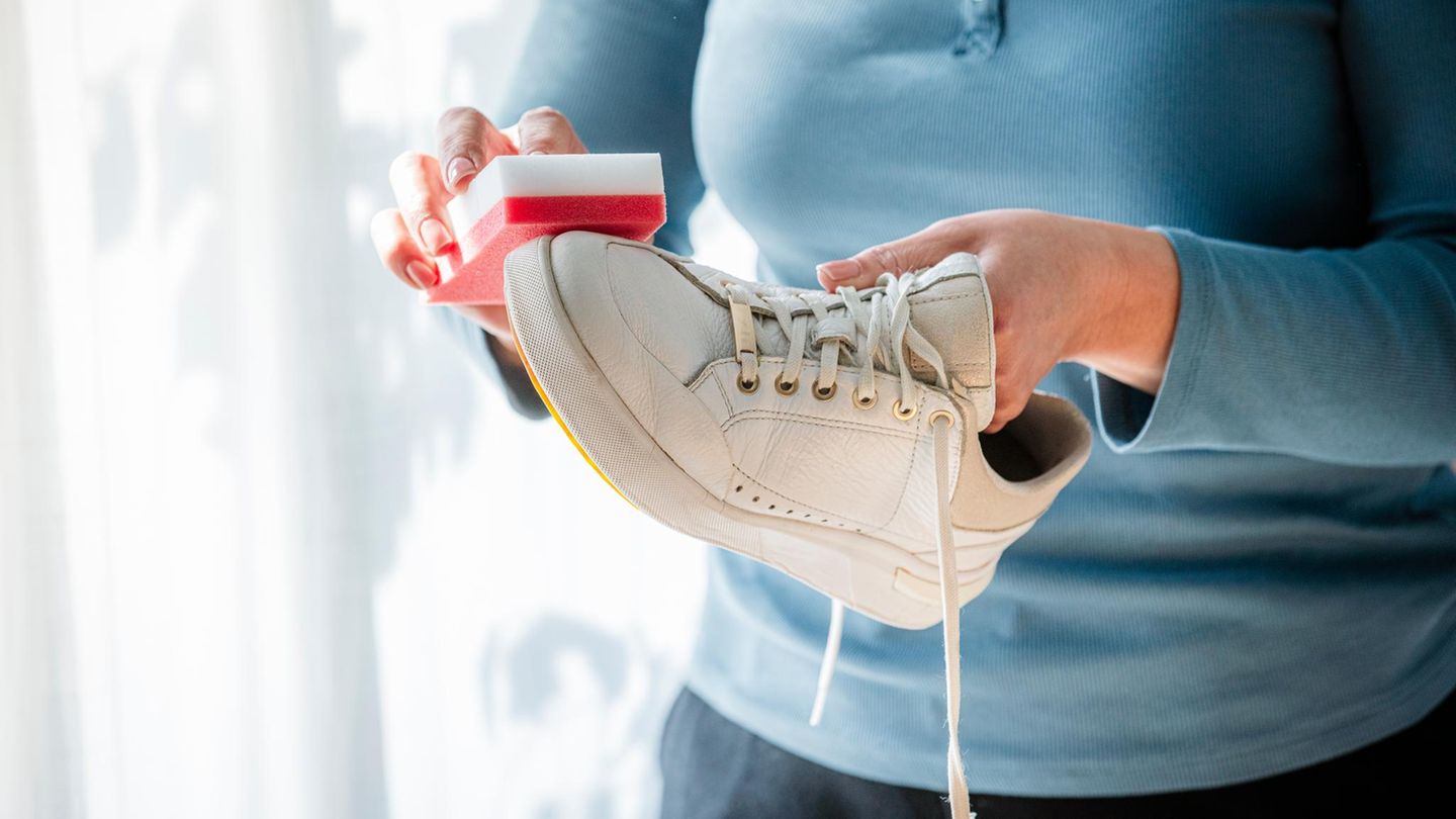 Frau, die weiße Turnschuhe zu Hause mit einem speziellen Reinigungsschwamm reinigt