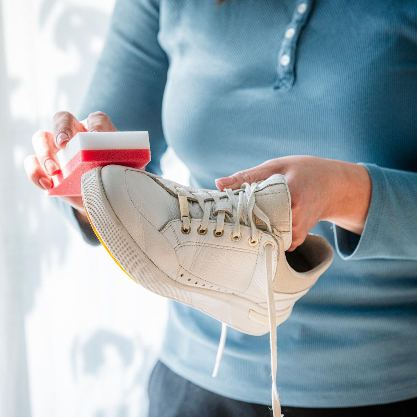 Frau, die weiße Turnschuhe zu Hause mit einem speziellen Reinigungsschwamm reinigt