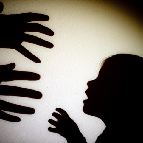 Schatten von Händen einer erwachsenen Person und der Kopf eines Kindes an einer Wand eines Zimmers