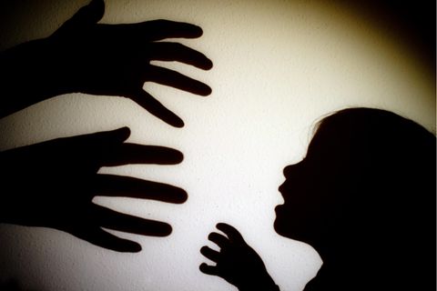 Schatten von Händen einer erwachsenen Person und der Kopf eines Kindes an einer Wand eines Zimmers