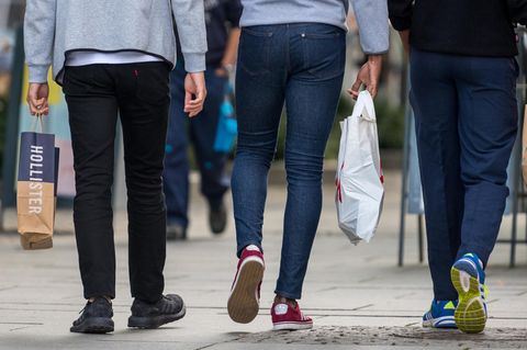 Drei Junge Männer mit Einkaufstaschen flanieren über eine Einkaufsmeile
