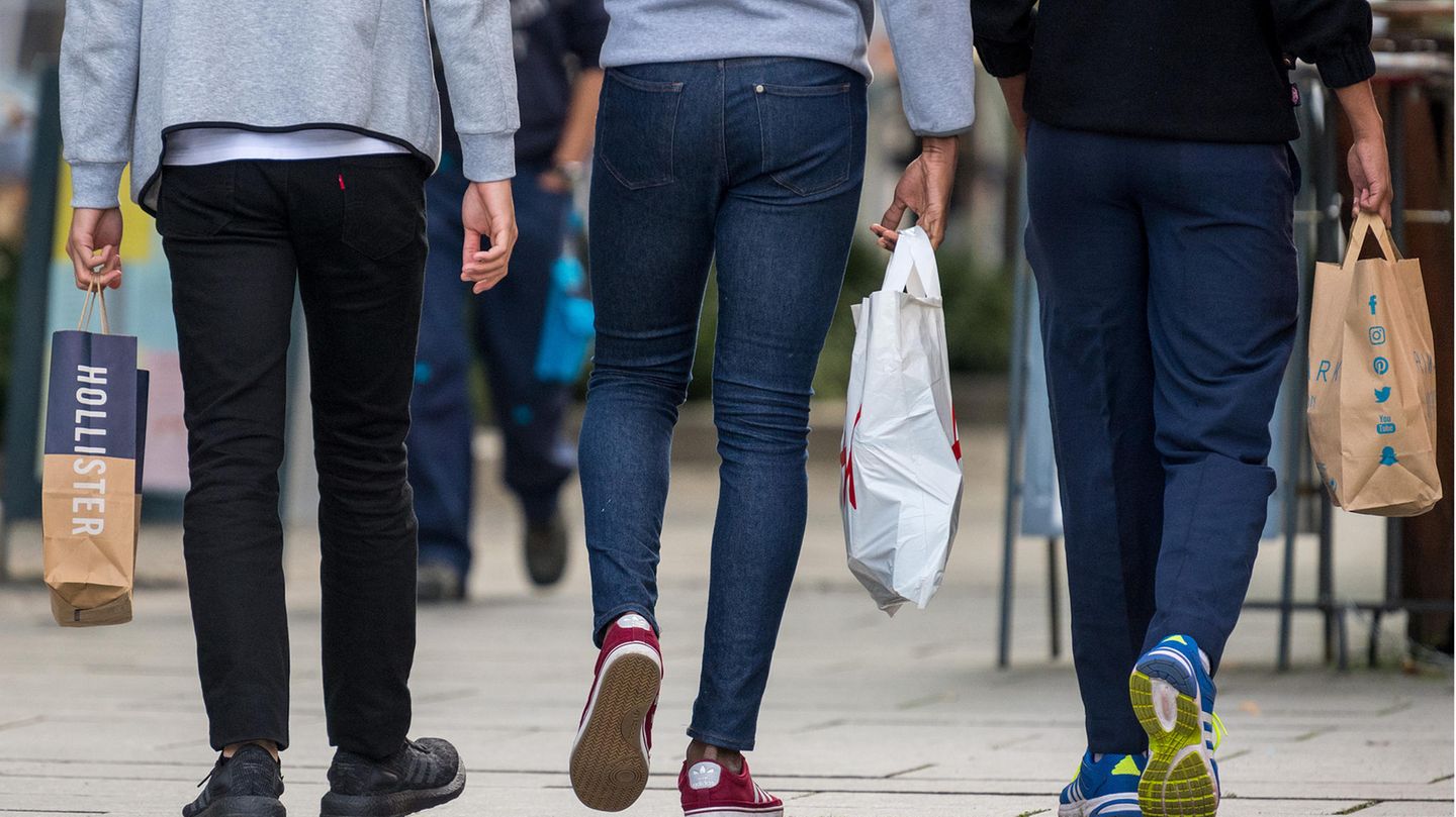 Drei Junge Männer mit Einkaufstaschen flanieren über eine Einkaufsmeile